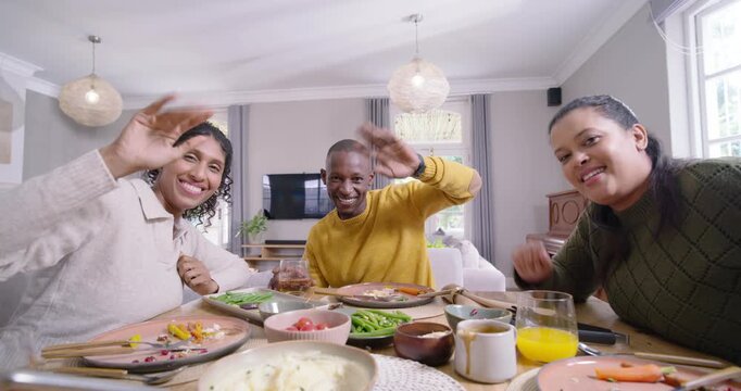 African American friends seeing camera on table at home, smiling, waving at camera, raising glasses