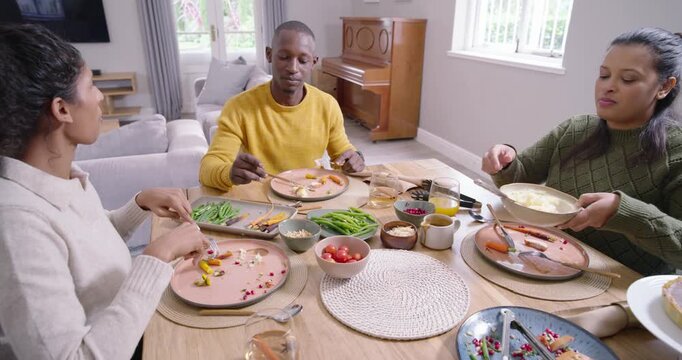 Family laughing, leading to passing bowls and scooping mashed spuds at home table sharing dinner