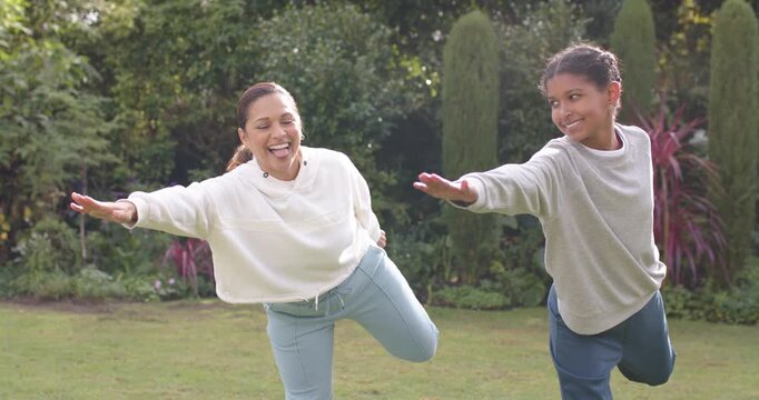 Mother and teenage daughter starting balance after warmup, holding one leg pose on garden lawn