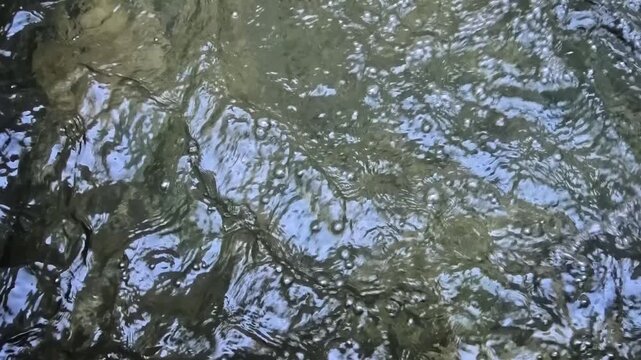 Vertical 1080p 240fps ultra slow motion video of fountain water ripples close up. Abstract top down shot of concentric liquid waves, fluid motion and sun light reflections texture background