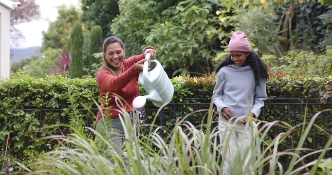 African American mother and child in yard, mom tipping green can, watering plants, teaching
