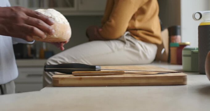 African American men entering holding loaf placing on board with knife preparing to cut at counter