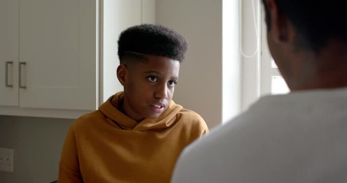 Teen male in mustard hoodie looking up softening smile listening at home while adult speaking right