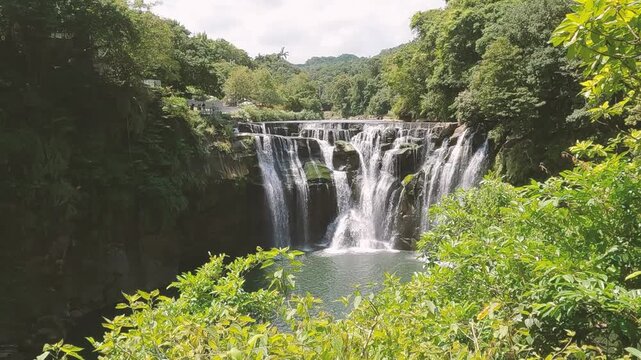 Horizontal 4K 120fps slow motion drone video of Shifen Waterfall in Taiwan. Scenic landscape shot with pan left camera movement revealing the powerful cascade, lush green nature and bright sunshine