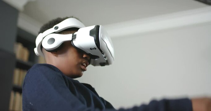 African American dad and son at home, son donning VR headset exploring while dad using tablet
