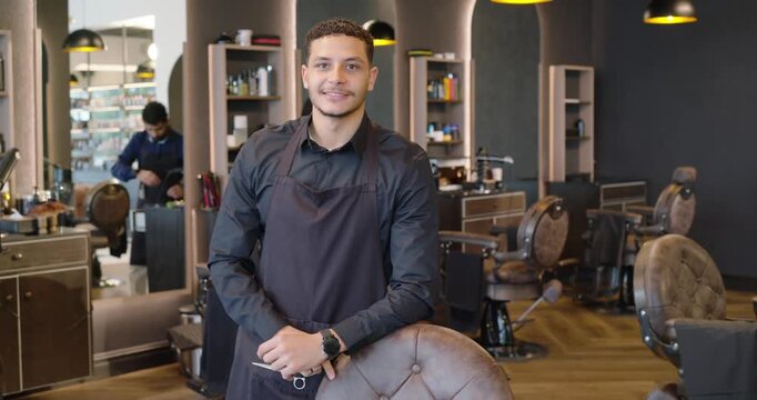 African American male barbers, lead barber black-aproned after trim posing holding scissors in shop