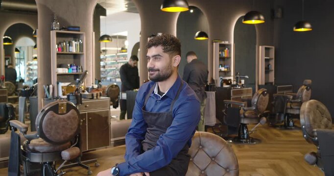 African American male coworkers, barber in tufted chair apron turning and smiling as camera zooming