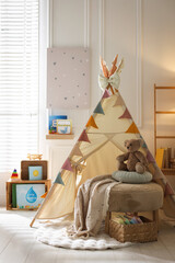 Beautiful wigwam, ottoman, different toys and books in child's room. Interior design © New Africa