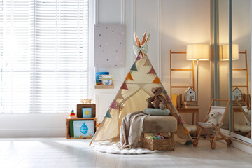 Beautiful wigwam, ottoman, different toys and books in child's room. Interior design © New Africa