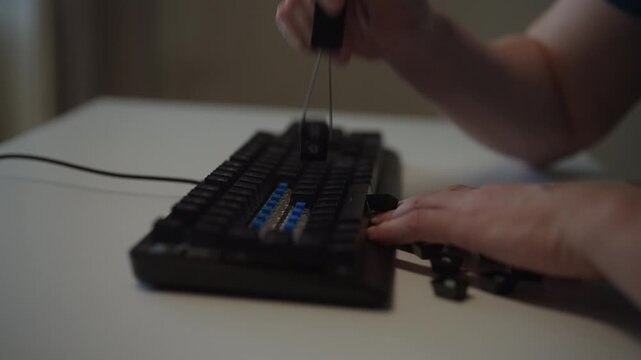 Close-up side view of person using keycap puller tool to remove keys from mechanical keyboard for cleaning, customizing, repair on white desk. Concept of underlying blue switches, slow motion