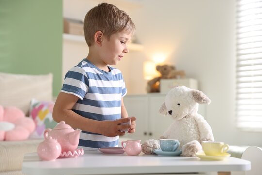 Little boy playing tea party with toy sheep at white table indoors