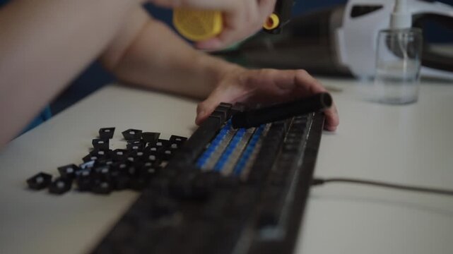Man hands using keycap puller to remove black keys from mechanical keyboard for cleaning and maintenance, with all keycaps lying on white desk beside it. Shooting in slow motion