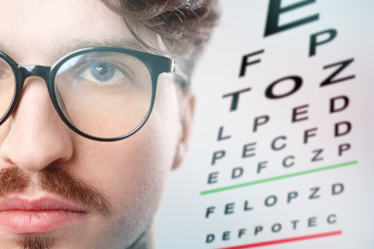Man in glasses and eye chart on white background, selective focus. Vision check