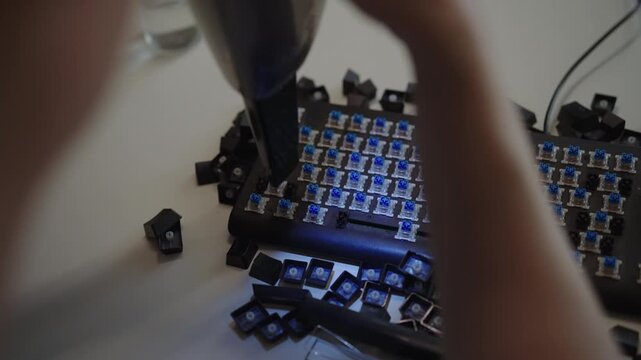 Focused technician using small vacuum cleaner to remove dust and debris from blue switches of disassembled mechanical keyboard, ensuring optimal performance and cleanliness. Shooting in slow motion