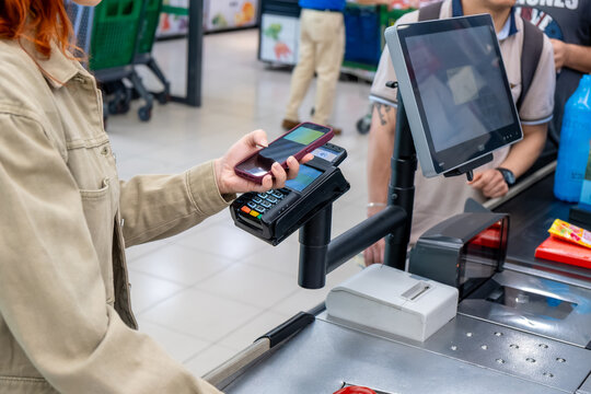 Woman making contactless payment using smartphone at supermarket checkout