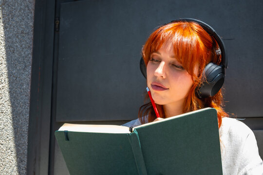 Redheaded woman thinking while writing in notebook
