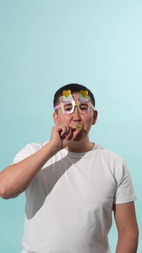 Man wearing funny party glasses blowing a shiny green noisemaker