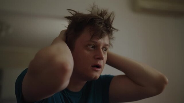 Distressed young man sitting at home, clutching head in despair and feeling overwhelmed. Concept of mental health crisis, anxiety attack, emotional turmoil from severe stress. Shooting in slow motion