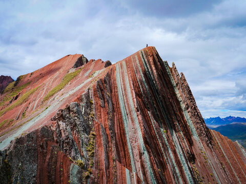 Stunning Rainbow Mountain in Peru with a hiker standing on the peak under a cloudy sky