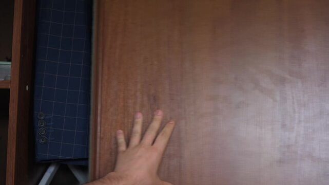 Close-up of a hand opening a closet where white shirts and a blue jacket are hanging