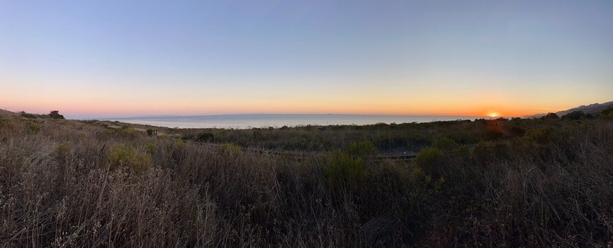 A breathtaking panoramic view capturing the fiery sunset over the coastal flora and the Pacific Ocean in Goleta, California.