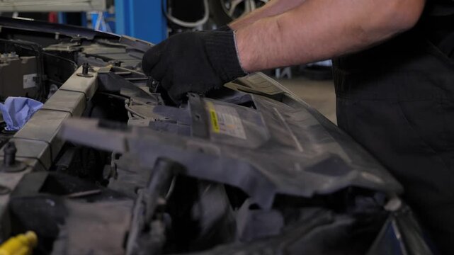 A technician carefully removes the plastic cover from the engine compartment before beginning the repair work at the garage.