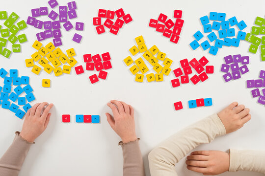 Scenic top down view of a creative primary school learning process. Children hands assembling word dominoes on white desk for interactive spelling lessons and cognitive growth.