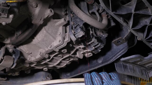 A detailed view of the underside of the vehicle after an oil change, with a stream of water at the service station. The mechanic is cleaning the underside of the car using a specialized tool.