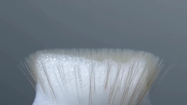 Close view of brush bristles with foam forming, blooming, settling, and receding on tip under soft studio light, revealing textured lather, clustered bubbles, and clean grooming detail