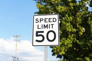 Fototapeta premium Speed limit 50 road sign against blue sky promotes safe driving and traffic awareness. Transportation safety background for urban streets road regulations and driver education.