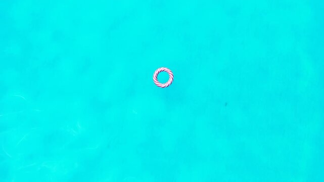 Overhead view of red and white striped inflatable ring floating on clear turquoise pool water, creating calm summer leisure scene with bright color contrast and minimal composition
