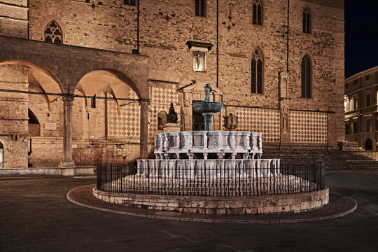Perugia, Umbria, Italy: night view of the fountain Fontana Maggiore, a masterpiece of medieval sculpture and the landmark monument of the city.. Behind, the ancient Cathedral