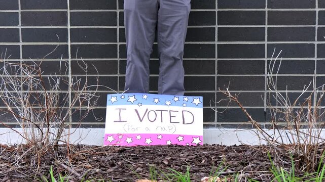 Man holding a humorous, satirical campaign sign reading I Voted for a nap, capturing themes of election fatigue, voting fatigue, and political burnout