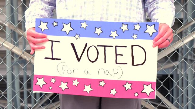 Man holding a humorous, satirical campaign sign reading I Voted for a nap, capturing themes of election fatigue, voting fatigue, and political burnout