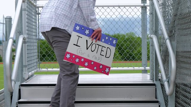 Man holding a humorous, satirical campaign sign reading I Voted for a nap, capturing themes of election fatigue, voting fatigue, and political burnout