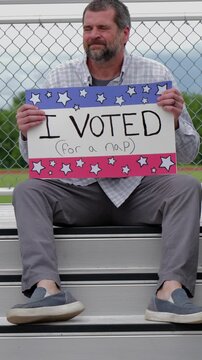 Man holding a humorous, satirical campaign sign reading I Voted for a nap, capturing themes of election fatigue, voting fatigue, and political burnout