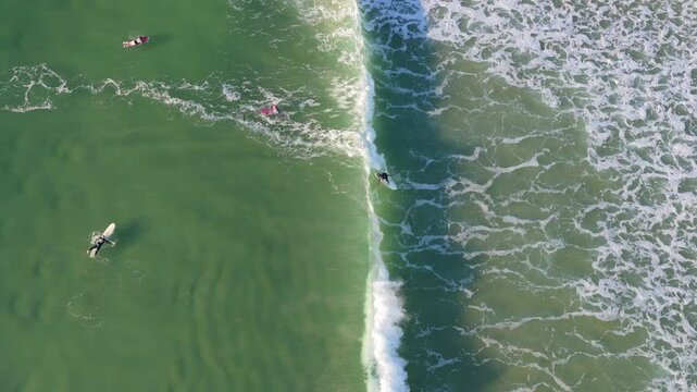 Semi-orbiting aerial drone shot moving from left to right above the surf break at Burleigh Headland with surfers riding waves on the Gold Coast, Queensland, Australia