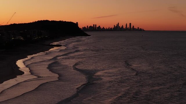 Slow forward push-in aerial drone shot approaching Burleigh Headland with the Surfers Paradise and Broadbeach skyline at twilight on the Gold Coast, Queensland, Australia