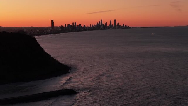 Forward dolly aerial drone shot approaching Burleigh Headland with the Surfers Paradise and Broadbeach skyline at twilight on the Gold Coast, Queensland, Australia