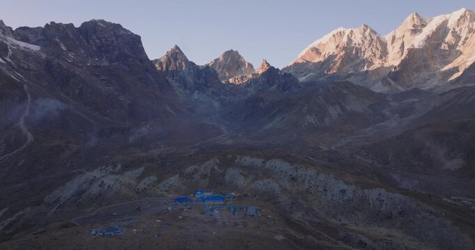 Dzongla village Everest region Nepal, aerial drone orbits small settlements with blue roofs situated in a high-altitude alpine valley surrounded by steep mountain ridges and rocky peaks