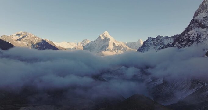 Everest region Nepal, aerial drone shot showing the high-altitude mountain peak of Ama Dablam with white clouds sprawling across its rocky and snowy slopes along the Three Passes Trek.
