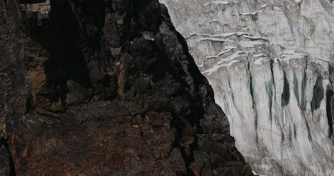 Cho Oyu mountain Everest region Nepal, aerial gliding shot past a brown rock cliff pillar reveals a highly textured and deeply layered glacial icefall structure in the background.
