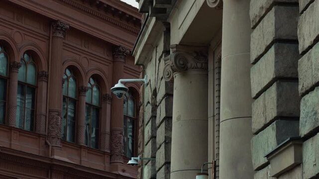 Ornate historic building facades with arched windows, carved columns, weathered stone details, and mounted security cameras creating contrast between classic architecture and modern surveillance