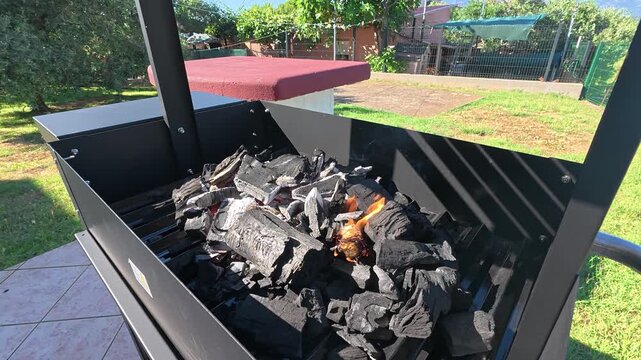 Charcoal briquettes inside a barbecue grill being ignited before cooking. Outdoor grilling preparation concept focused on barbecue setup, heat generation, and summer cooking.