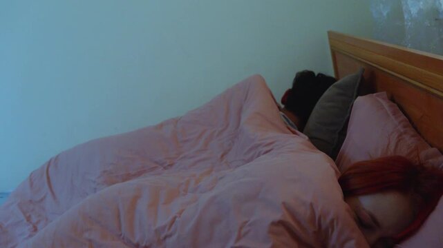 Young couple going to sleep in bed as man pulls blanket over his head