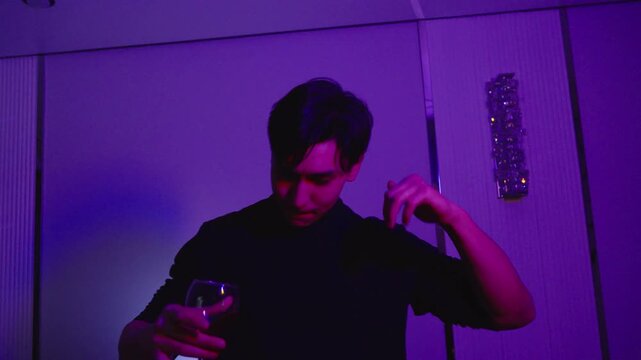 Young man dancing with a glass of red wine under changing lights