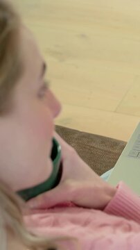 Vertical video: Laptop showing woman viewing marks on sofa green headset pink knit, copy space