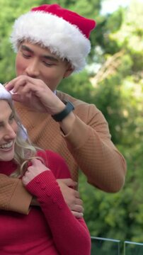 Vertical video: Starting backhug man hugging woman in red knit on glass rail tapping Santa hats