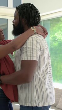 Vertical video: Embracing couple reuniting, swaying near glass door at home, wearing rust blouse
