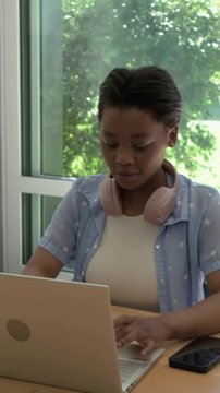 Vertical video: Typing student looking up as mentor entering to help, pointing at laptop by window
